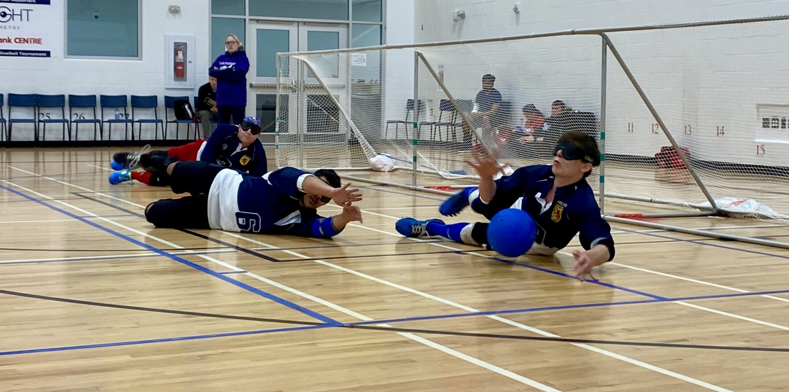 Three people in position in front of the long net to block an incoming goalball.